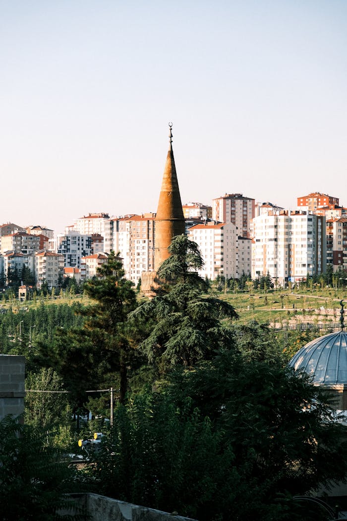 A historic minaret stands tall against a backdrop of modern apartments in an urban setting.